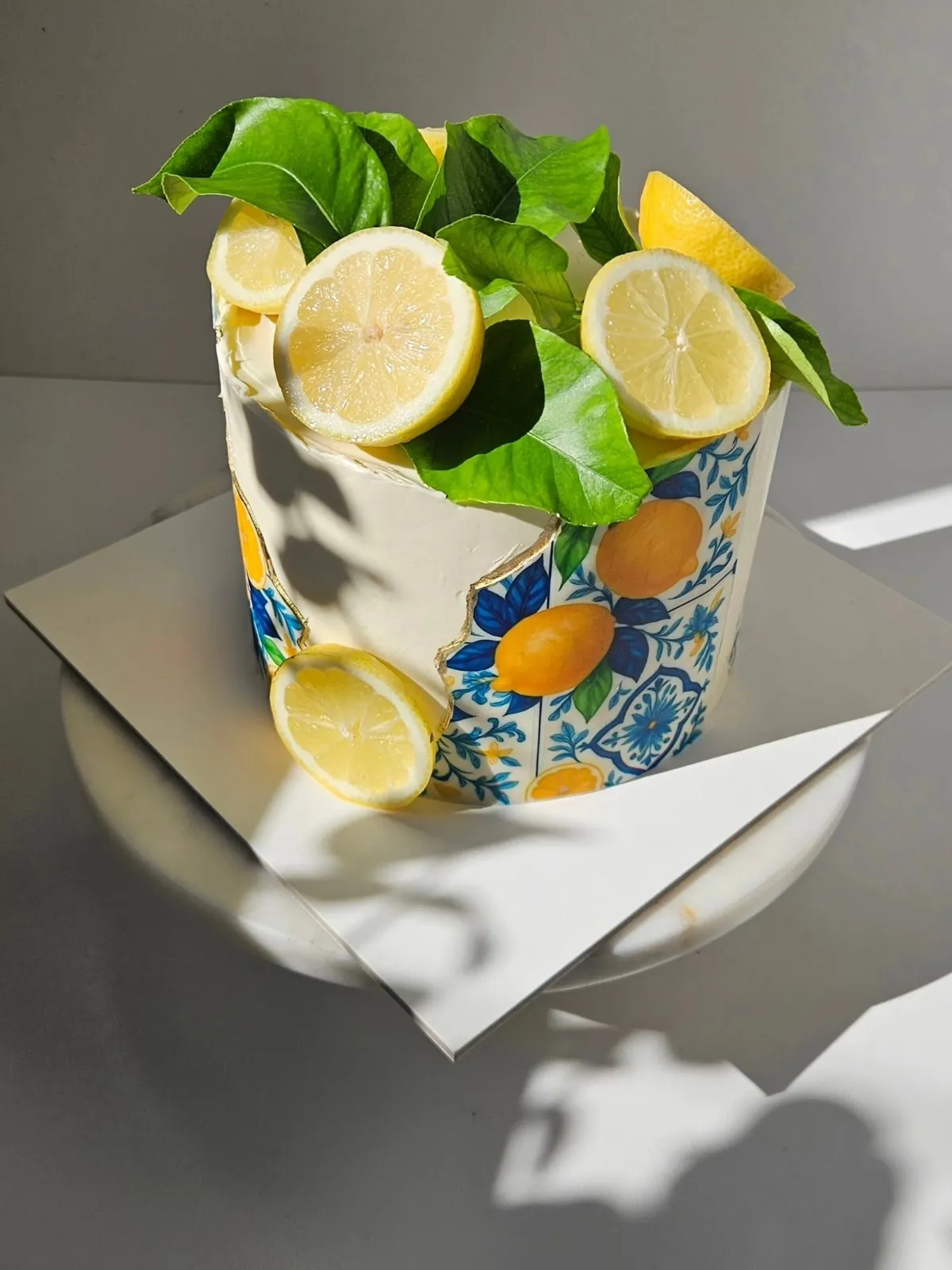 Balta kūka ar citronu šķēlēm, citronkoka lapām un zili dzeltenu flīžu raksta ēdamdruku